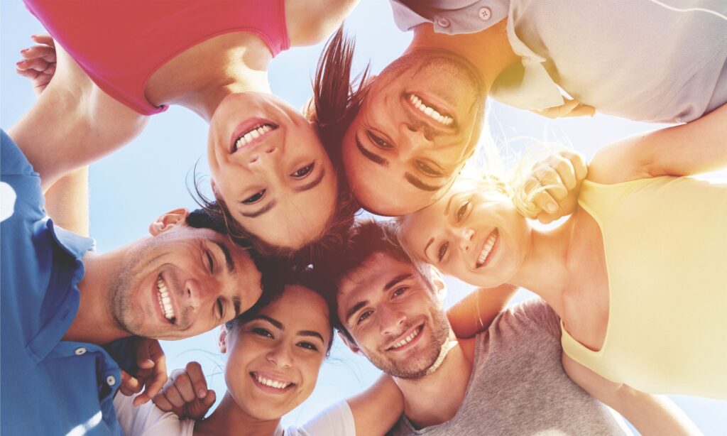 View looking up at group of people huddled together smiling under blue sky